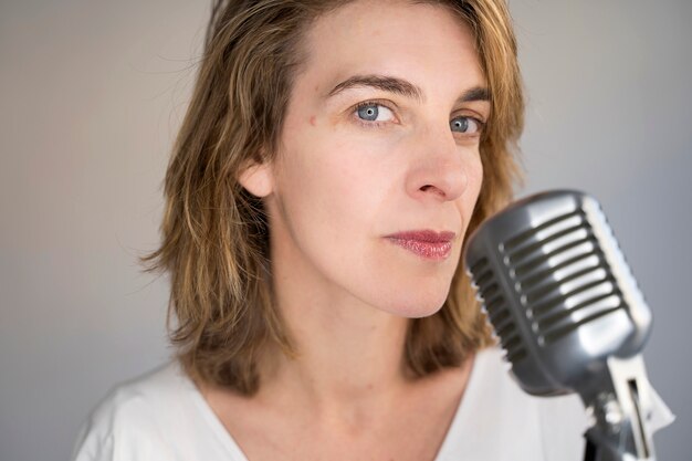 Photo portrait of serious caucasian woman singing a song with a vintage silver microphone. woman holding a vintage microphone and performing live music.