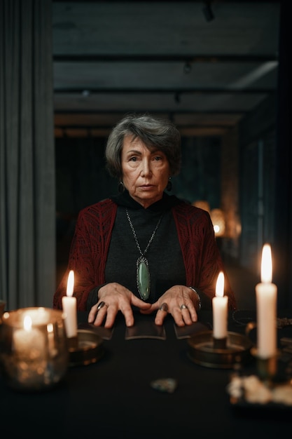 Portrait of serious confident fortune teller holding crystal pendant over candle light for divination seance