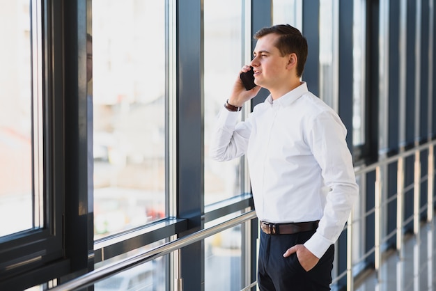 Portrait of a serious confident man boss having mobile phone conversation while resting after meeting with his partners, businessman talking on cell telephone while standing in modern space indoors