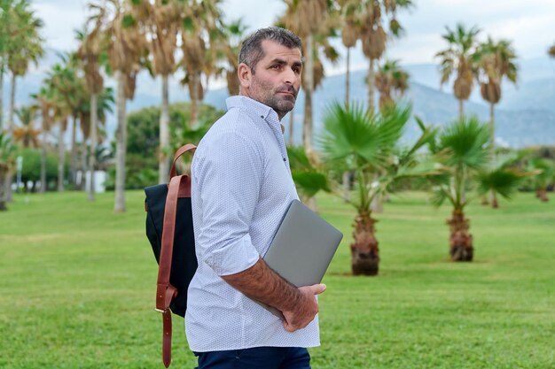 Portrait of serious confident mature man with laptop outdoors