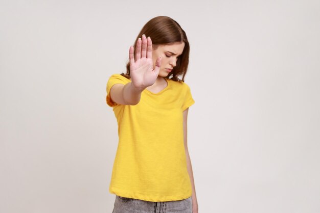 Portrait of serious confident teenager girl showing stop gesture with palm of hand rejecting stress and problems no discrimination Indoor studio shot isolated on gray background