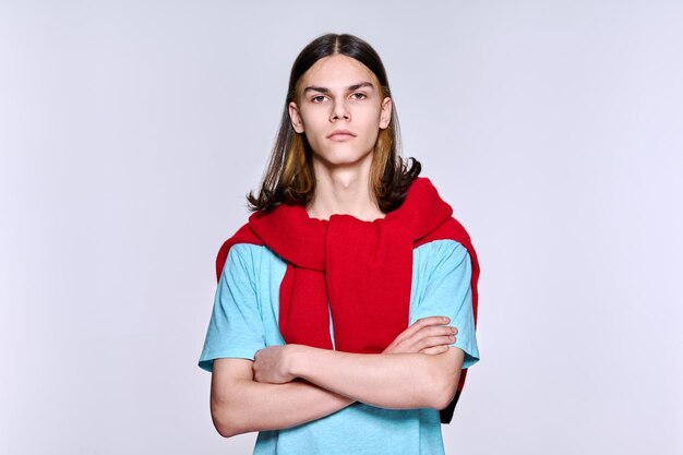 Portrait of serious confident young male with folded hands looking at camera light background