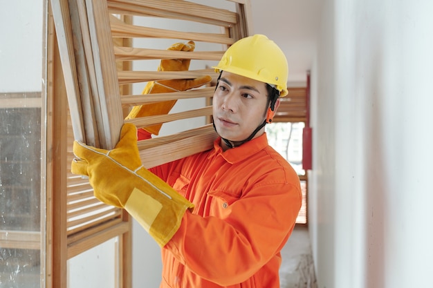 Портрет серьезного строителя с тяжелыми деревянными решетками, идущего по коридору в доме