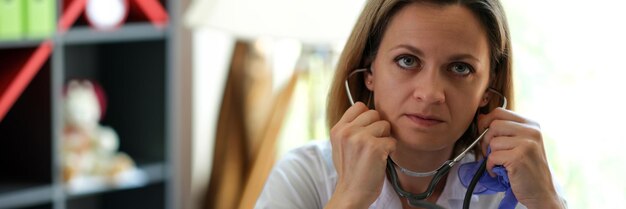 Foto ritratto di medico femminile serio che posa nell'ufficio della clinica con lo sguardo del praticante dello stetoscopio