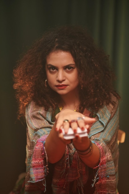 Portrait of serious fortune teller asking client to take tarot card from her hands