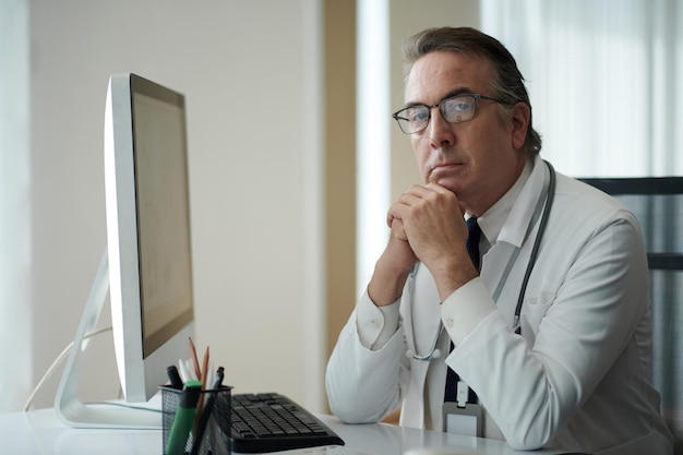 Portrait of serious general practitioner working on computer at his desk