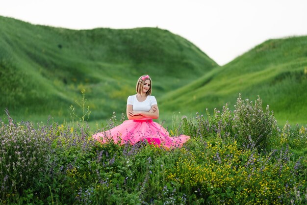 Portrait of a serious girl princess in a country The girl in a pink dress walks barefoot on the green grass in the field