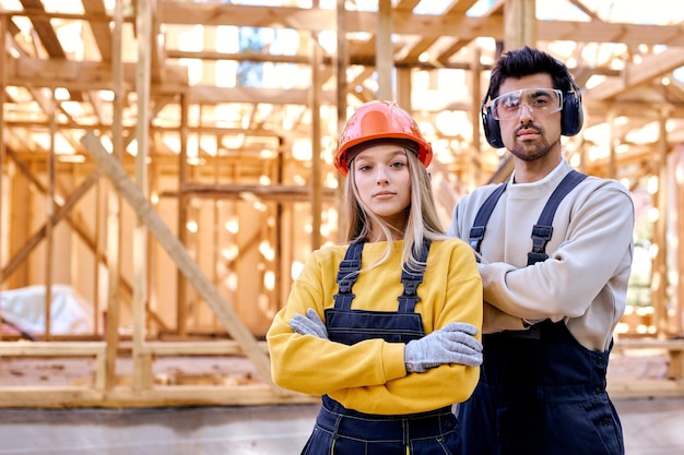 Portrait of serious male and female construction comrades posing at camera outdoors