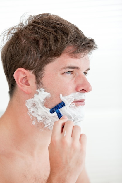 portrait of a serious man shaving looking away standing in the bathroom