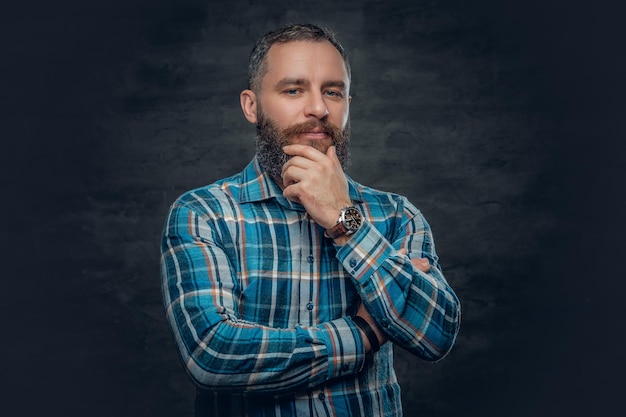 Portrait of serious middle age bearded male dressed in plaid flannel shirt over grey background.