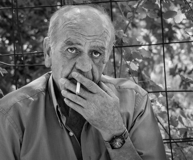 Photo portrait of a serious old greek retired male who smokes a cigarette in black and white in greece