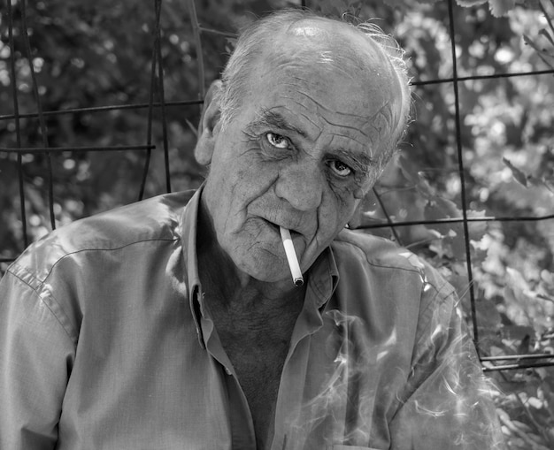 Photo portrait of a serious old greek retired male who smokes a cigarette with a smile in black and white