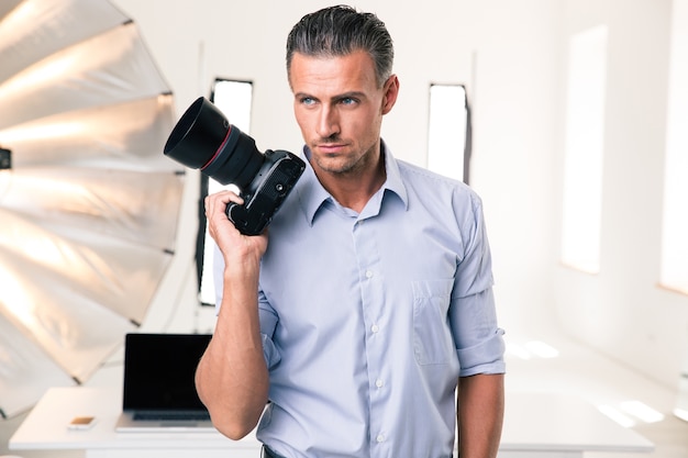 Portrait of a serious photographer holding camera in studip