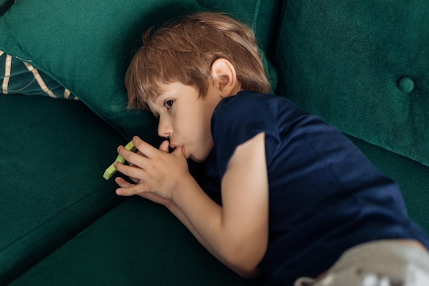 Portrait of serious scary sad and depressed little boy lying on green sofa sucking thumb finger Children stuttering