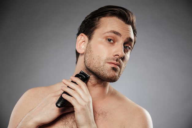 portrait of a serious shirtless man shaving beard