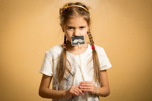 Photo portrait of serious small girl posing with decorative mustache