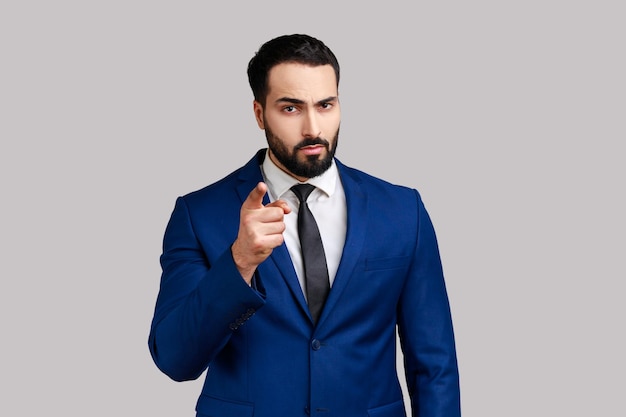 Portrait of serious strict bearded man standing with admonishing gesture, scolding for mistake and warning, wearing official style suit. Indoor studio shot isolated on gray background.