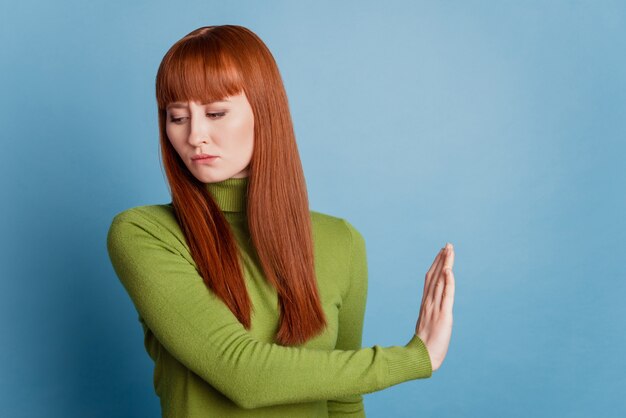 Portrait of serious strict girl hand show stop gesture sad look side on blue background