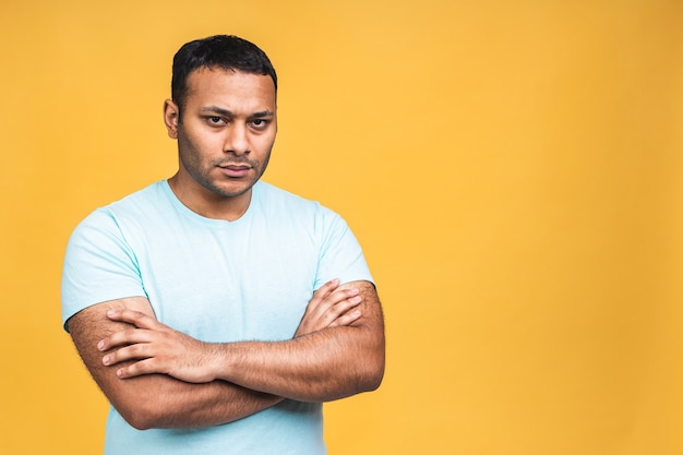 Photo portrait of a serious thinking young african american indian black man standing isolated over yellow background.