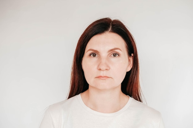 Portrait of a serious woman dressed in casual white t shirt poses indoor on a white background