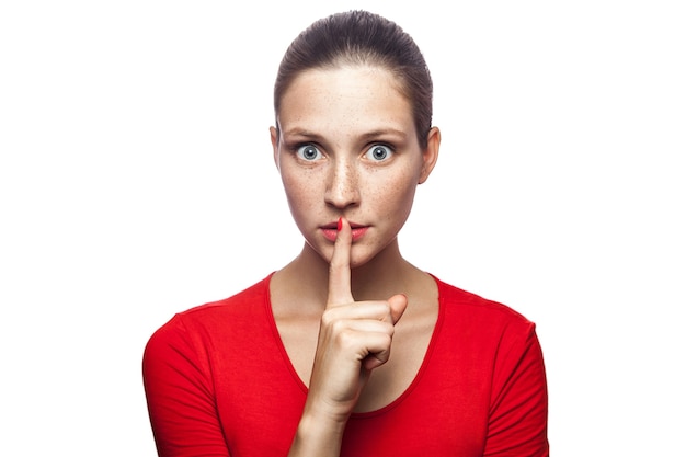 Portrait of serious woman in red tshirt with freckles with shh sign on her lips