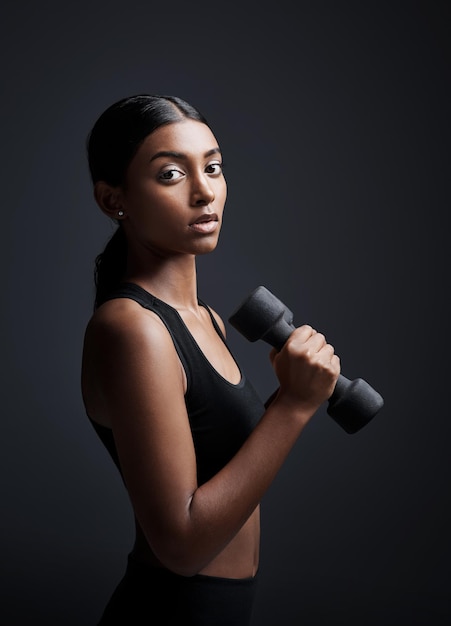 Серьезный портрет и женщина с гантелями для упражнений в студии на черном фоне