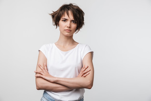 Portrait of serious woman with short brown hair in basic t-shirt frowning  isolated over white wall