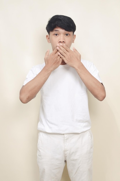 Портрет серьезного молодого азиата, показывающего знак молчания на изолированном фоне