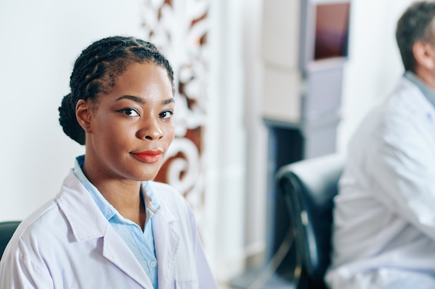 Ritratto di giovane medico femminile nero serio nello sguardo del camice