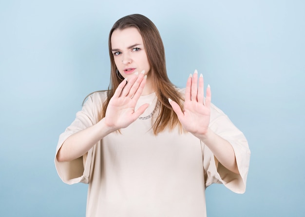 Portrait of serious young european woman standing with arms outstretched showing stop gesture isolated on blue wall