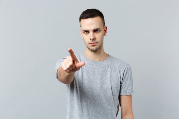 Portrait of serious young man in casual clothes pointing index finger at front