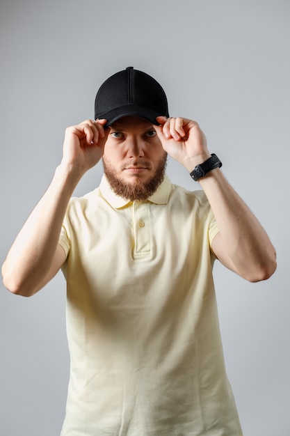 Photo portrait of serious young man in a yellow t-shirt and black cap on gray.