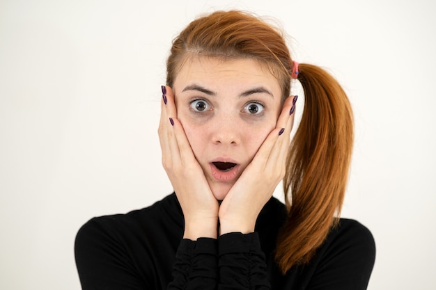 Photo portrait of serious young woman holding her hands to face thinking concentrated about something.