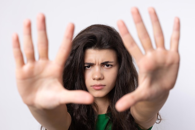 Portrait of a serious young woman showing stop gesture with her palm over white background