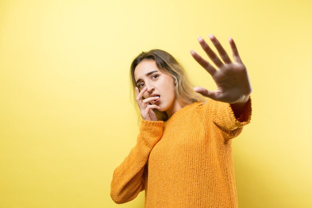 Portrait of a serious young woman showing stop gesture with her\
palm over yellow background