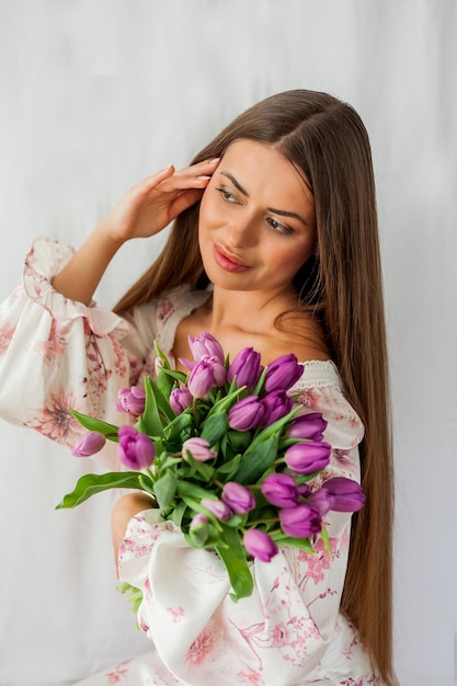 Portrait of sexy beautiful young woman with long hair Model with a bouquet of lilac tulips on white Spring Holidays