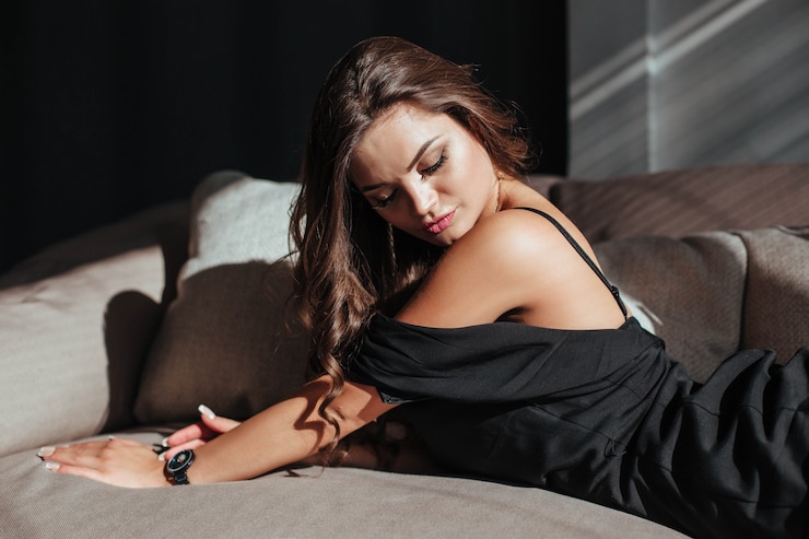 Photo portrait of a sexy brunette in a black dress on a dark background girl takes off her dress slowly in