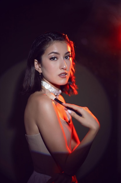 Portrait of a sexy fashionable makeup artist woman in a white skirt with a black powder brush and box stands in the studio red light background