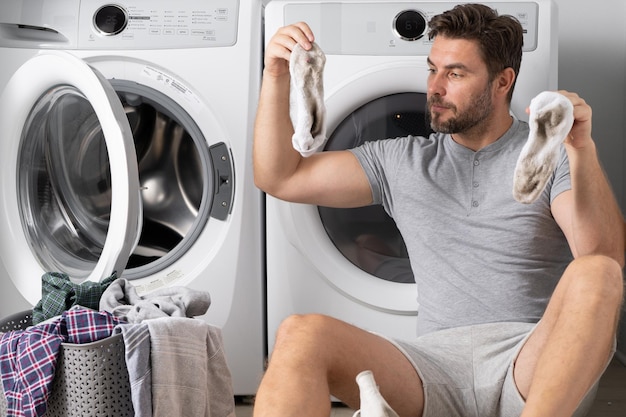 Portrait of sexy man with dirty clothes near washing machine handsome man sits in front of washing m