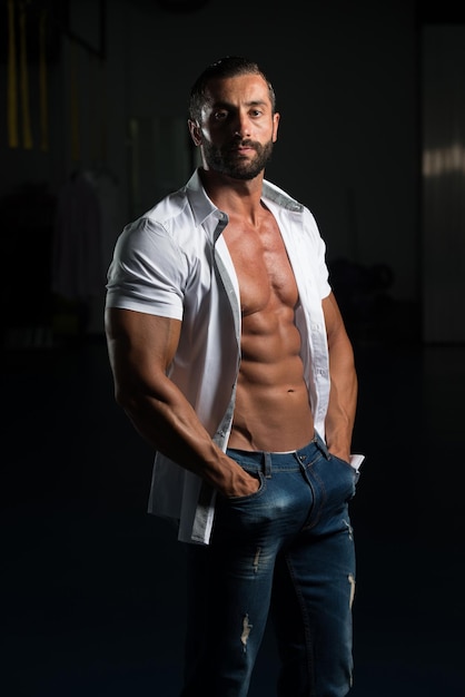 Портрет сексуального мускулистого мужчины в брюках и рубашке позирует