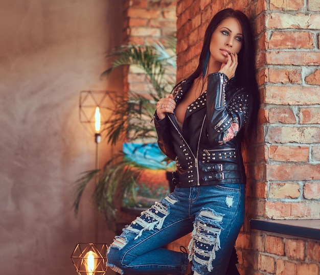 portrait of a sexy sensual brunette posing in stylish leather jacket and jeans leaning against a brick wall.