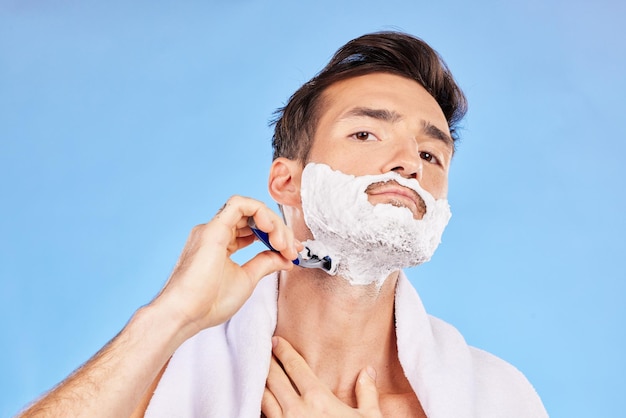 Portrait shave and bathroom with a man model shaving his face in studio on a blue background for grooming beauty skincare and shaving foam with a handsome young male using a razor in the morning