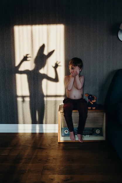 Photo portrait of shirtless boy sitting against shadow on wall