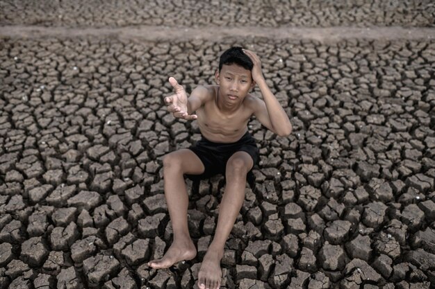 Photo portrait of shirtless boy sitting on cracked land