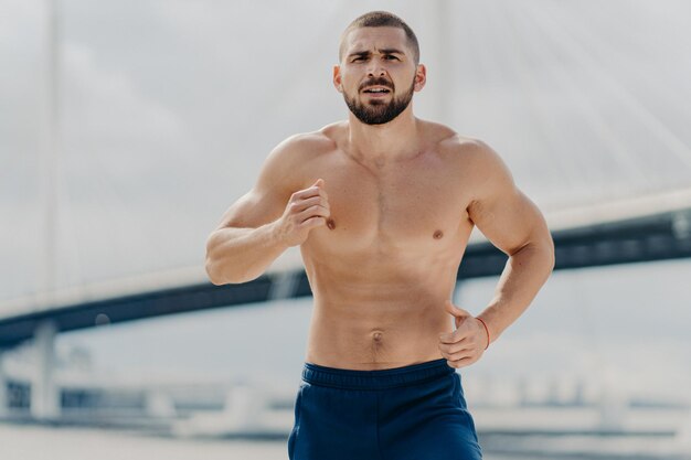 Portrait of shirtless man exercising against bridge