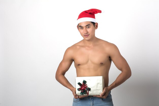 Portrait of shirtless man holding christmas present against white background