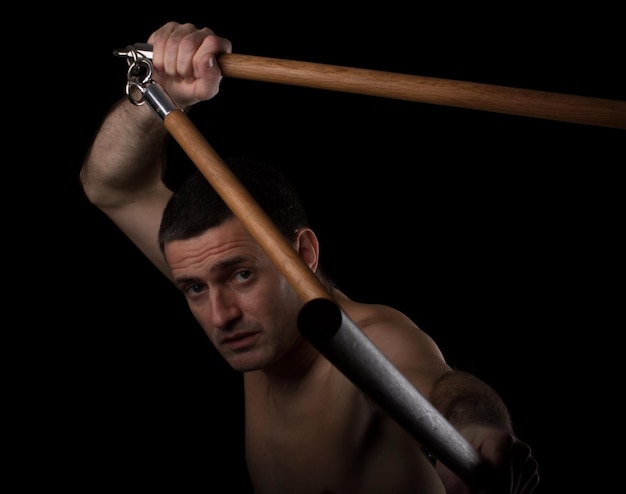 Portrait of shirtless man holding weapon against black background