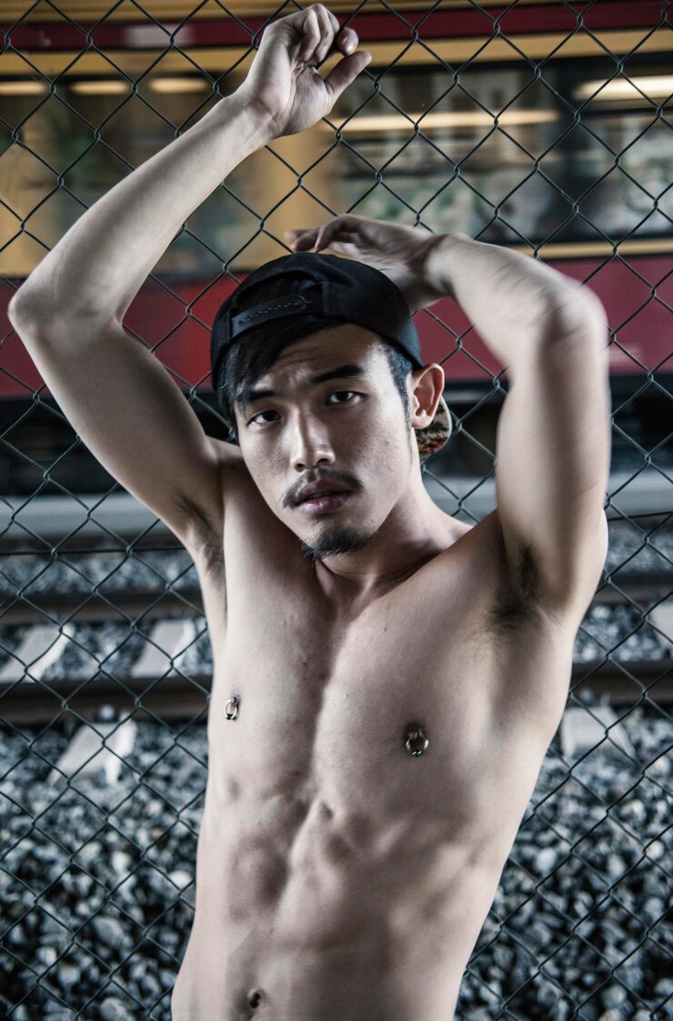 Photo portrait of shirtless man leaning on chainlink fence against train