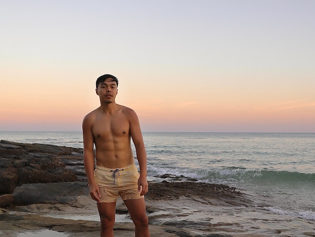 Photo portrait of shirtless man standing at beach against clear sky during sunset