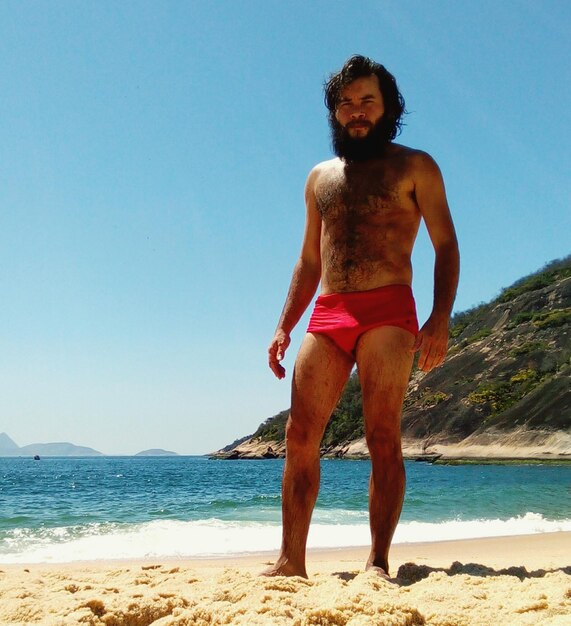 Portrait of shirtless man standing at beach during sunny day